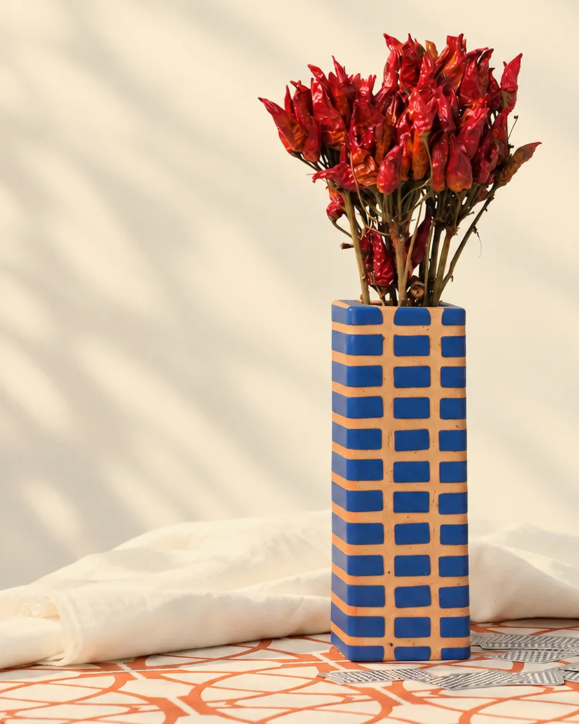 Vaso a colonna con intarsi blu e cotto, con un mazzo di peperoncini rossi secchi, su un tavolo decorato in cotto.