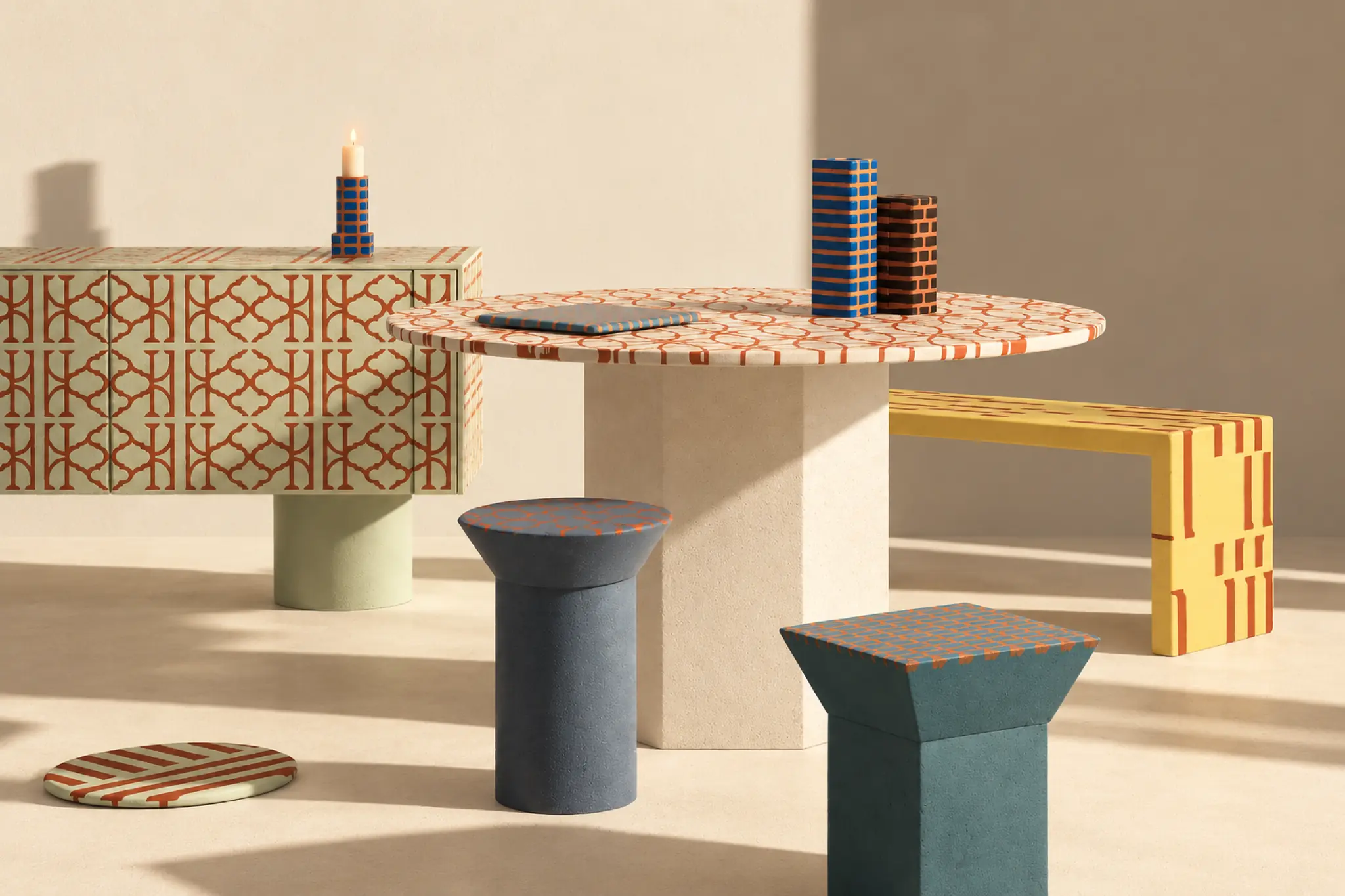 Arredi della collezione Due Sicilie in un interno dai toni caldi: una madia, un tavolo rotondo, una panca e due sgabelli con decori geometrici in cotto.